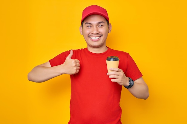 Portrait d'un jeune homme de messagerie asiatique souriant tenant une tasse de café en papier montrant le signe du geste du pouce vers le haut isolé sur fond jaune
