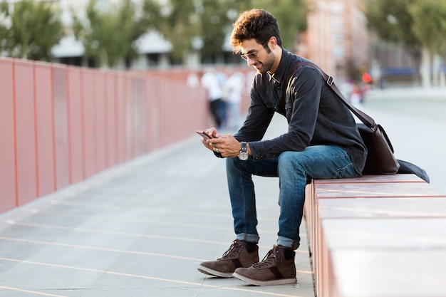 Portrait de jeune homme moderne utilisant son téléphone portable dans la rue.