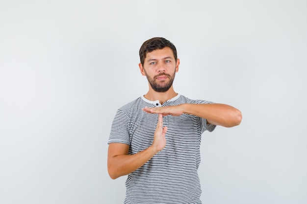 Portrait de jeune homme montrant un geste de pause dans le temps en t-shirt rayé et à la vue de face confiant