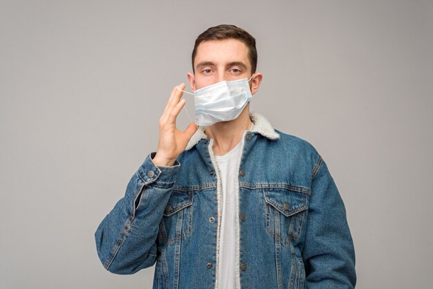 Portrait d'un jeune homme, sur un mur clair, avec un masque de protection sur le visage. Prévention du coronavirus, grippe.