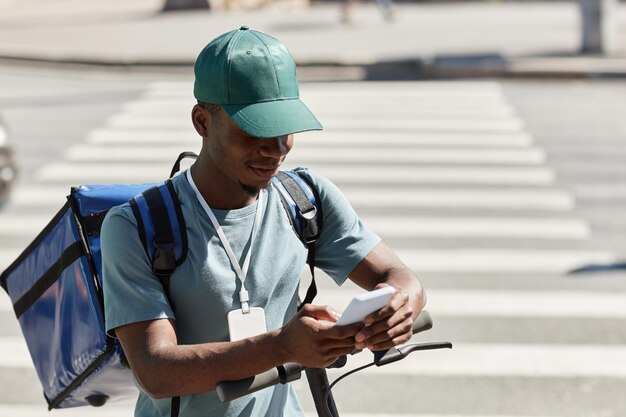 Portrait de jeune homme noir utilisant un smartphone tout en livrant de la nourriture dans l'espace de copie de la ville