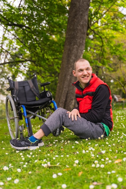 Portrait d'un jeune homme paralysé assis sur l'herbe à côté du fauteuil roulant une marguerite fleurs souriant dans la nature