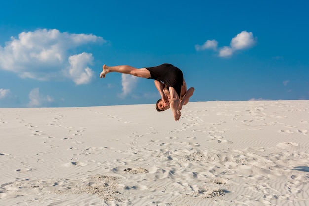 Portrait d'un jeune homme de parkour faisant un saut périlleux ou un saut périlleux sur le sable.
