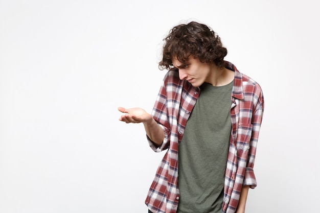 Portrait d'un jeune homme perplexe en vêtements décontractés debout, regardant sous la main avec quelque chose d'isolé sur fond de mur blanc en studio. Les gens émotions sincères, concept de style de vie. Maquette de l'espace de copie.