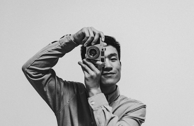 Portrait d'un jeune homme photographiant avec un appareil photo sur un fond gris