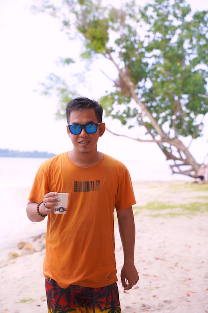 Photo portrait d'un jeune homme portant des lunettes de soleil alors qu'il se tient sur la plage