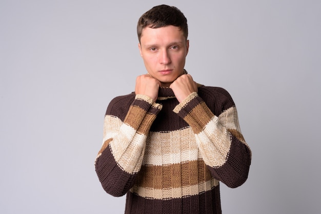 Portrait de jeune homme portant un pull à col roulé prêt pour l'hiver contre le mur blanc