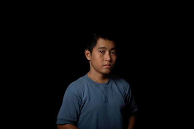 Portrait d'un jeune homme portant un t-shirt bleu regardant la caméra sur l'espace de copie de fond noir