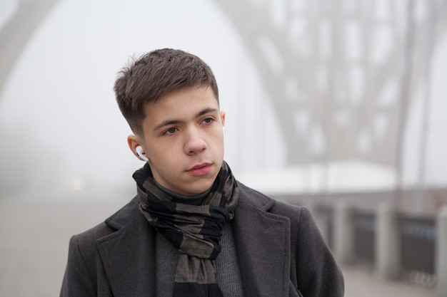 Photo portrait d'un jeune homme sur une promenade de la ville, temps d'hiver brumeux. photo dans les tons gris