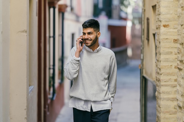 Portrait d'un jeune homme de race blanche dans des vêtements modernes parlant au mobile dans la rue