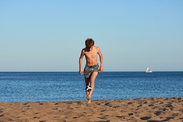 Un portrait d'un jeune homme de race blanche en forme de frapper un ballon sur la plage