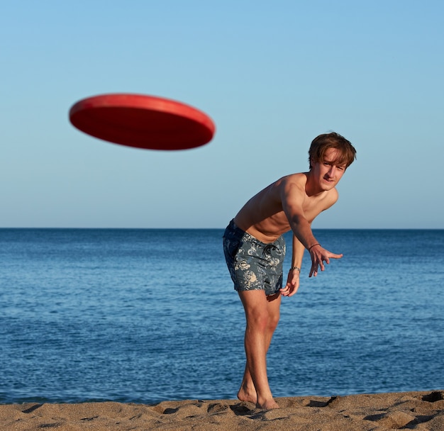 Un portrait d'un jeune homme de race blanche en forme jouant au frisbee sur la plage