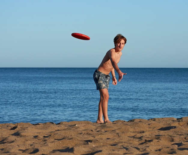 Un portrait d'un jeune homme de race blanche en forme jouant au frisbee sur la plage