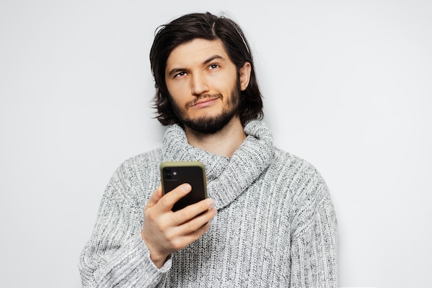 Portrait de jeune homme réfléchi avec smartphone en mains blanches.