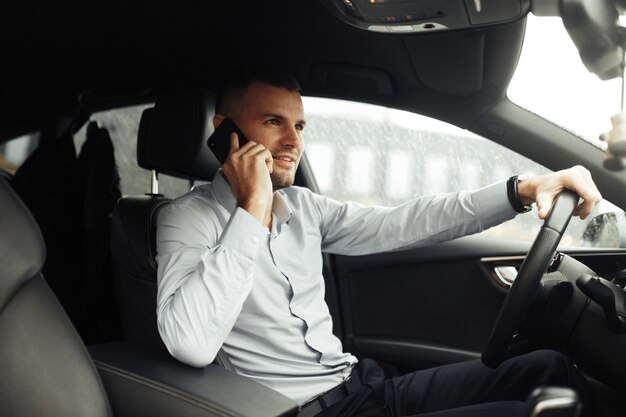 Portrait d'un jeune homme réussi dans la voiture. Conversations et appels téléphoniques, négociations.