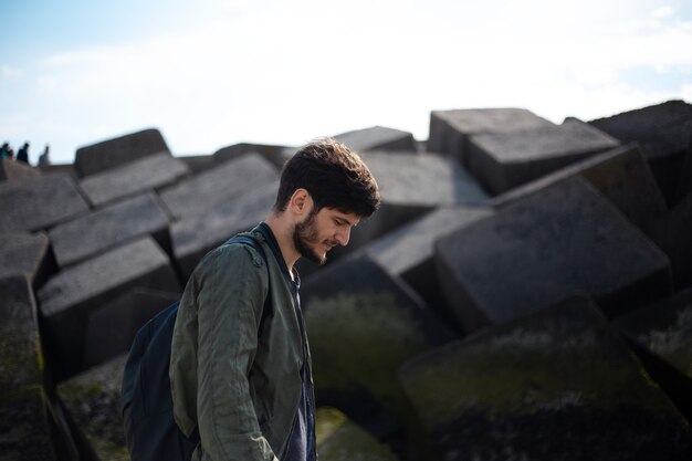 Portrait de jeune homme avec sac à dos sur de grosses pierres carrées.