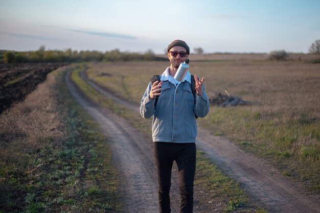 Portrait de jeune homme avec sac à dos tenant une bouteille d'eau thermo en aluminium réutilisable dans la main