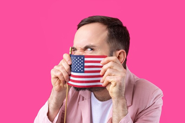 Portrait d'un jeune homme satisfait avec une barbe avec un drapeau américain sur un fond de studio rouge Grand patriote américain et défenseur de la liberté