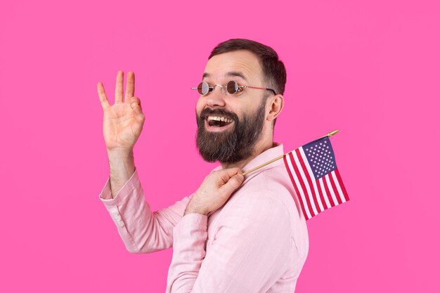 Portrait d'un jeune homme satisfait avec une barbe avec un drapeau américain sur un fond de studio rouge Grand patriote américain et défenseur de la liberté