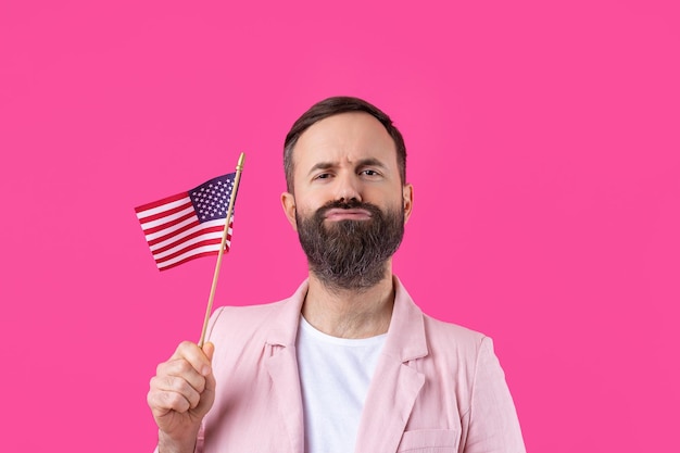 Portrait d'un jeune homme satisfait avec une barbe avec un drapeau américain sur un fond de studio rouge Grand patriote américain et défenseur de la liberté