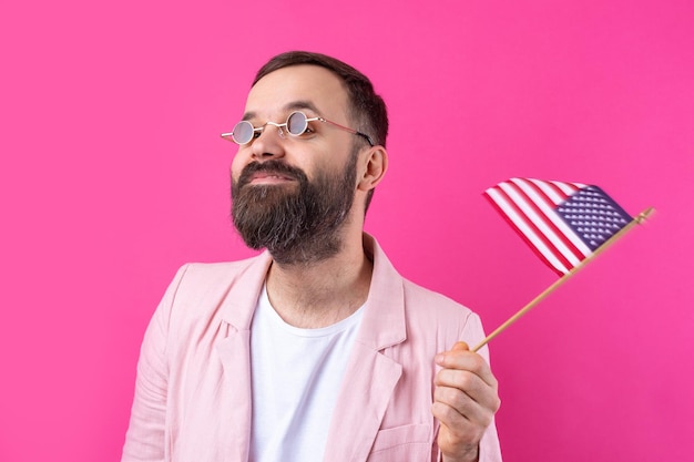 Portrait d'un jeune homme satisfait avec une barbe avec un drapeau américain sur un fond de studio rouge Grand patriote américain et défenseur de la liberté