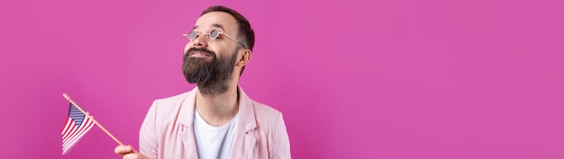 Portrait d'un jeune homme satisfait avec une barbe avec un drapeau américain sur un fond de studio rouge Grand patriote américain et défenseur de la liberté