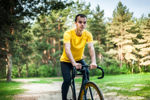 Portrait d'un jeune homme se déplaçant à vélo dans un parc public parmi les arbres et la végétation