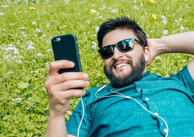 Portrait de jeune homme se détendre sur l'herbe et à l'aide de smartphone