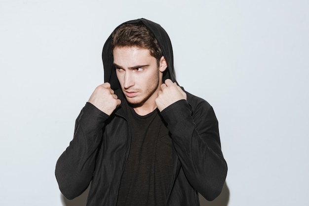 Portrait de jeune homme séduisant vêtu d'un t-shirt noir et d'un manteau debout sur fond blanc et posant.