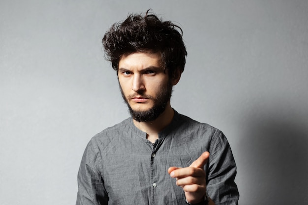 Portrait de jeune homme sérieux barbu aux cheveux ébouriffés, ayant une nouvelle idée, pointant le doigt loin.