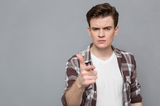 Portrait d'un jeune homme sérieux et confiant en conflit montrant une chemise à carreaux pointant sur vous