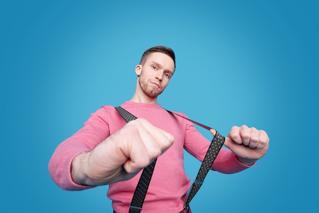 Portrait de jeune homme sérieux en pull rose tirant des bretelles de pantalon