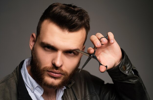 Portrait de jeune homme sexy d'un type avec des ciseaux de barbier pour un barbier barbier moderne se rasant un bel homme avec une coiffure moderne sur noir