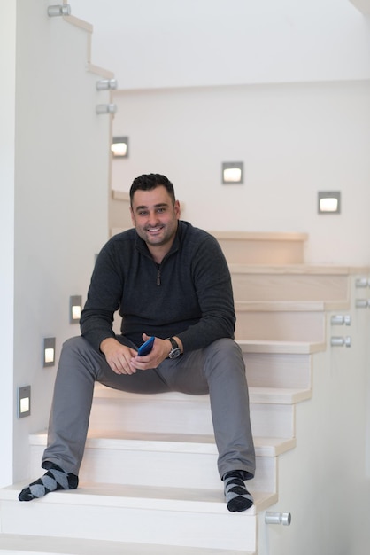 portrait d'un jeune homme souriant assis dans les escaliers avec un téléphone portable dans les mains