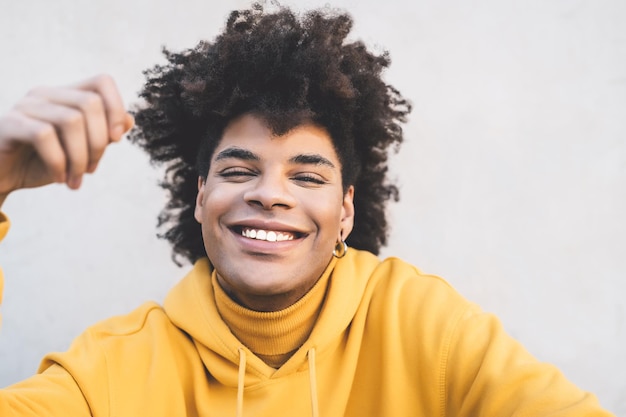 Photo portrait d'un jeune homme souriant aux cheveux bouclés assis contre le mur