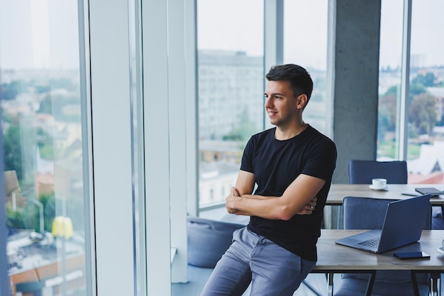 Portrait d'un jeune homme souriant dans un t-shirt noir dans le contexte d'un bureau moderne