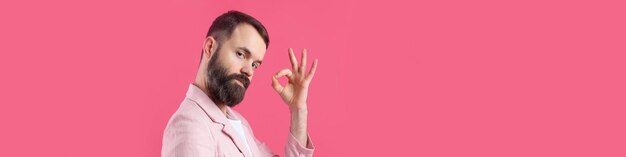 Portrait d'un jeune homme souriant dans une veste rose Homme montrant un geste ok en se tenant debout en studio sur fond rouge isolé