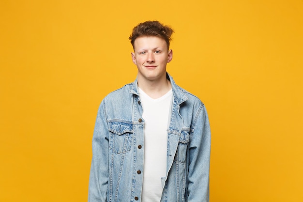 Portrait d'un jeune homme souriant dans des vêtements décontractés en denim debout et regardant la caméra isolée sur fond de mur orange jaune en studio. Émotions sincères des gens, concept de style de vie. Maquette de l'espace de copie.