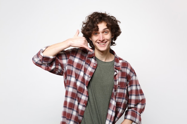 Portrait de jeune homme souriant dans des vêtements décontractés faisant un geste de téléphone comme dit de me rappeler isolé sur fond de mur blanc en studio. Les gens émotions sincères, concept de style de vie. Maquette de l'espace de copie.