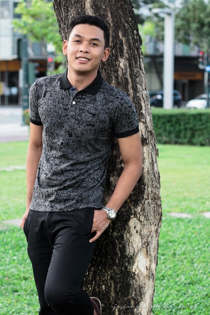 Photo portrait d'un jeune homme souriant debout contre un arbre dans un parc