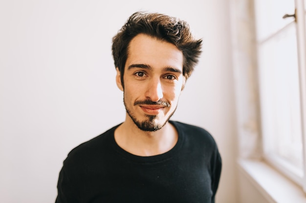 Portrait d'un jeune homme souriant devant la fenêtre de sa maison.