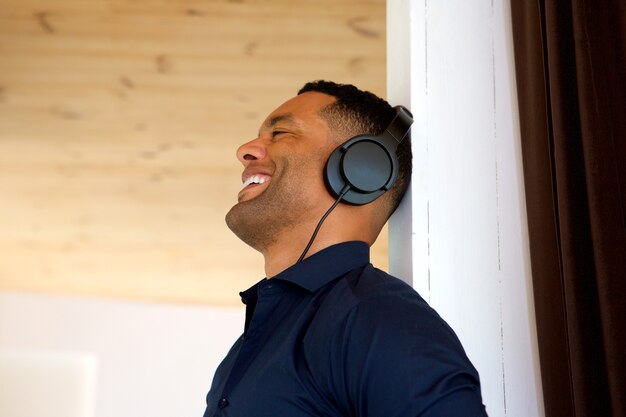 Portrait de jeune homme souriant, écoutant de la musique avec des écouteurs à la maison