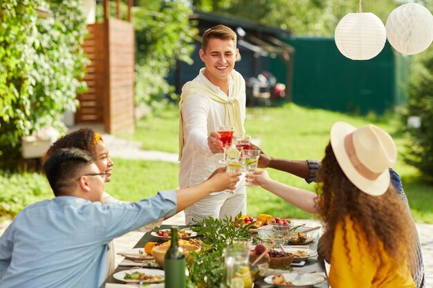 Portrait de jeune homme souriant, grillage avec des amis tout en appréciant le dîner sur la terrasse en été