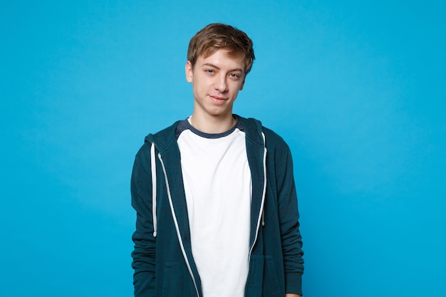 Portrait d'un jeune homme souriant séduisant dans des vêtements décontractés, debout isolé sur un mur bleu. Les gens émotions sincères, concept de style de vie.