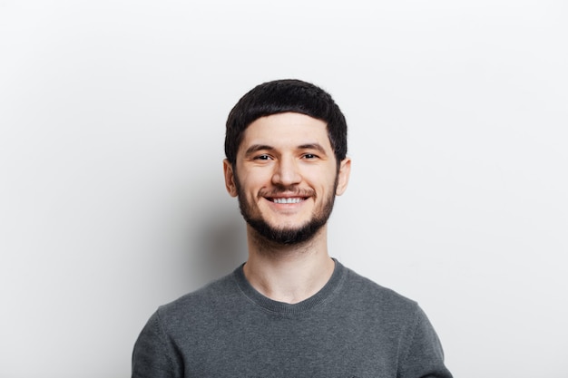 Portrait de jeune homme souriant sur une surface blanche.