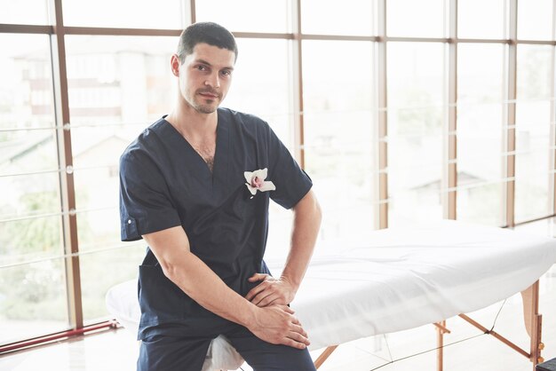 Portrait de jeune homme souriant en uniforme près de canapés de massage