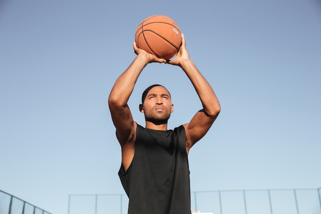 Portrait de jeune homme sportif sautant avec le basket-ball sur l'aire de jeux