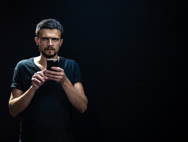 Portrait d'un jeune homme avec un téléphone dans ses mains dans l'obscurité.