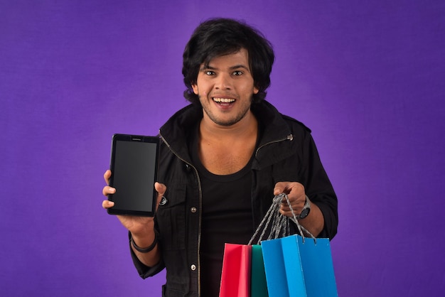 Portrait d'un jeune homme avec un téléphone portable ou une tablette smartphone et des sacs à provisions dans ses mains