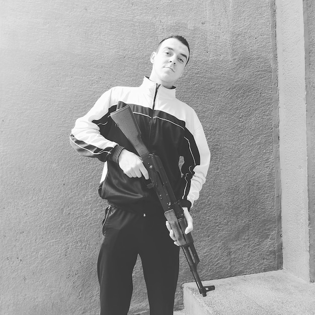 Portrait d'un jeune homme tenant un fusil alors qu'il se tient contre le mur